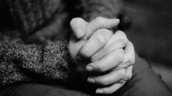 Nahaufnahme von zwei Händen, die ineinander verschränkt sind, vor einem unscharfen Hintergrund.