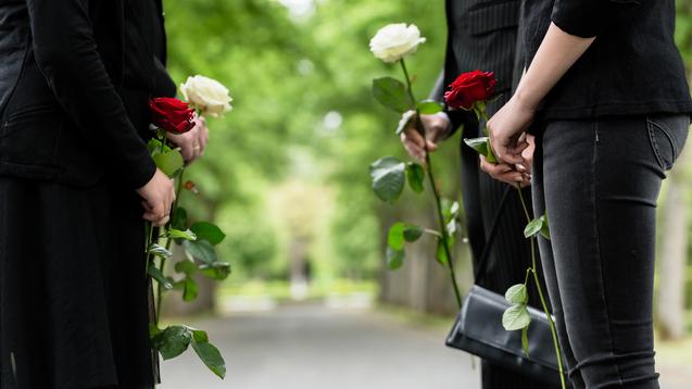 Vier Personen halten Rosen in einer parkähnlichen Umgebung, zwei rote und zwei weiße Blumen.